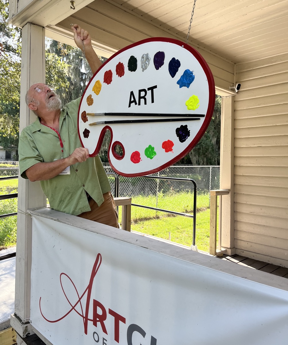 A volunteer hanging the Art Guild's palette-shaped ART sign at the gallery entrance